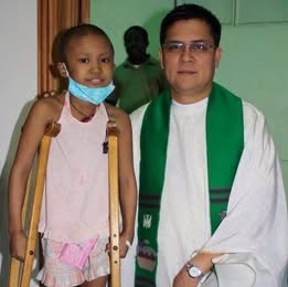 Fr. Arnold Abelardo standing beside a child using crutches